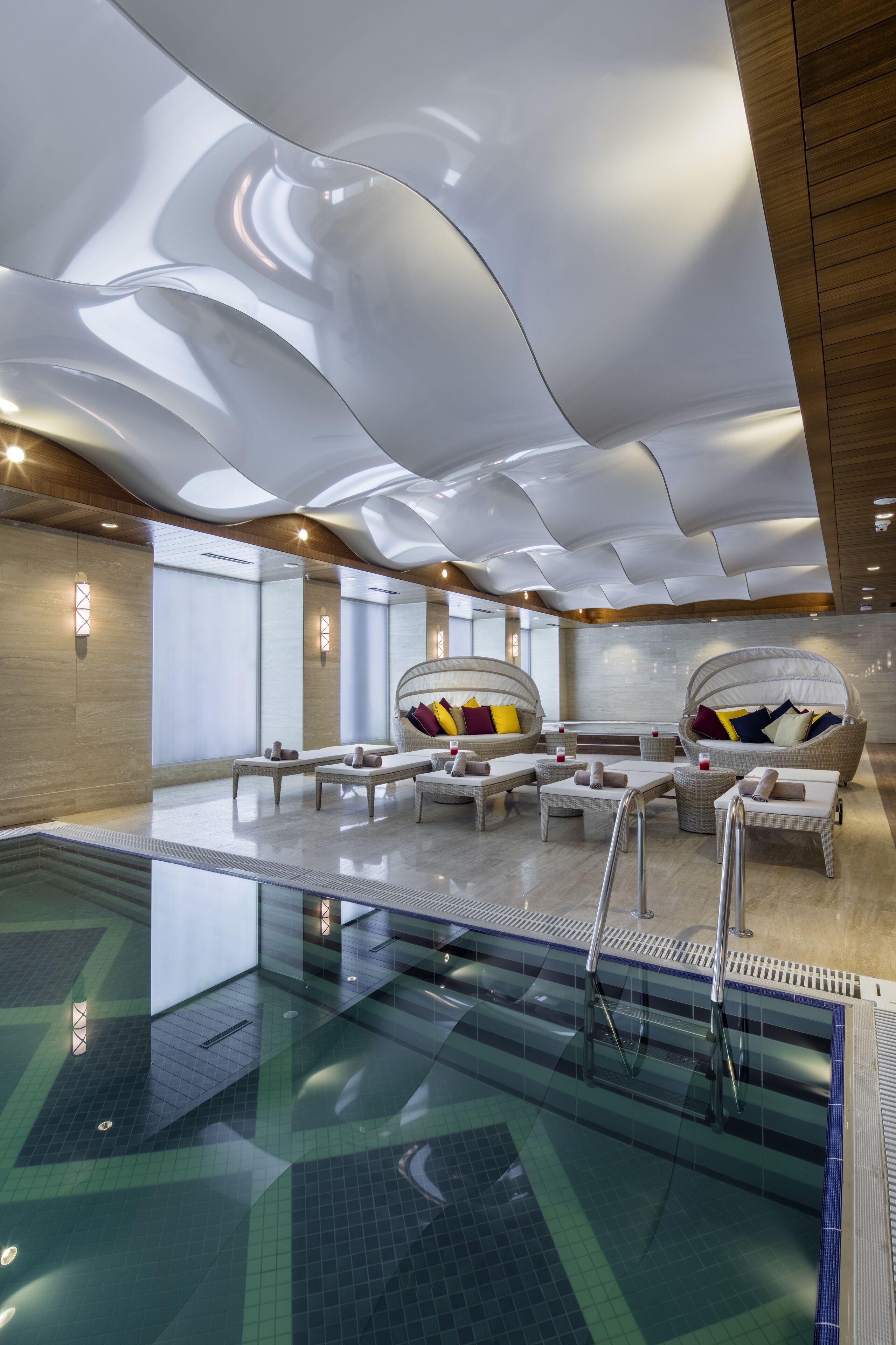A modern indoor swimming pool area with lounge chairs and a glass-enclosed pool.