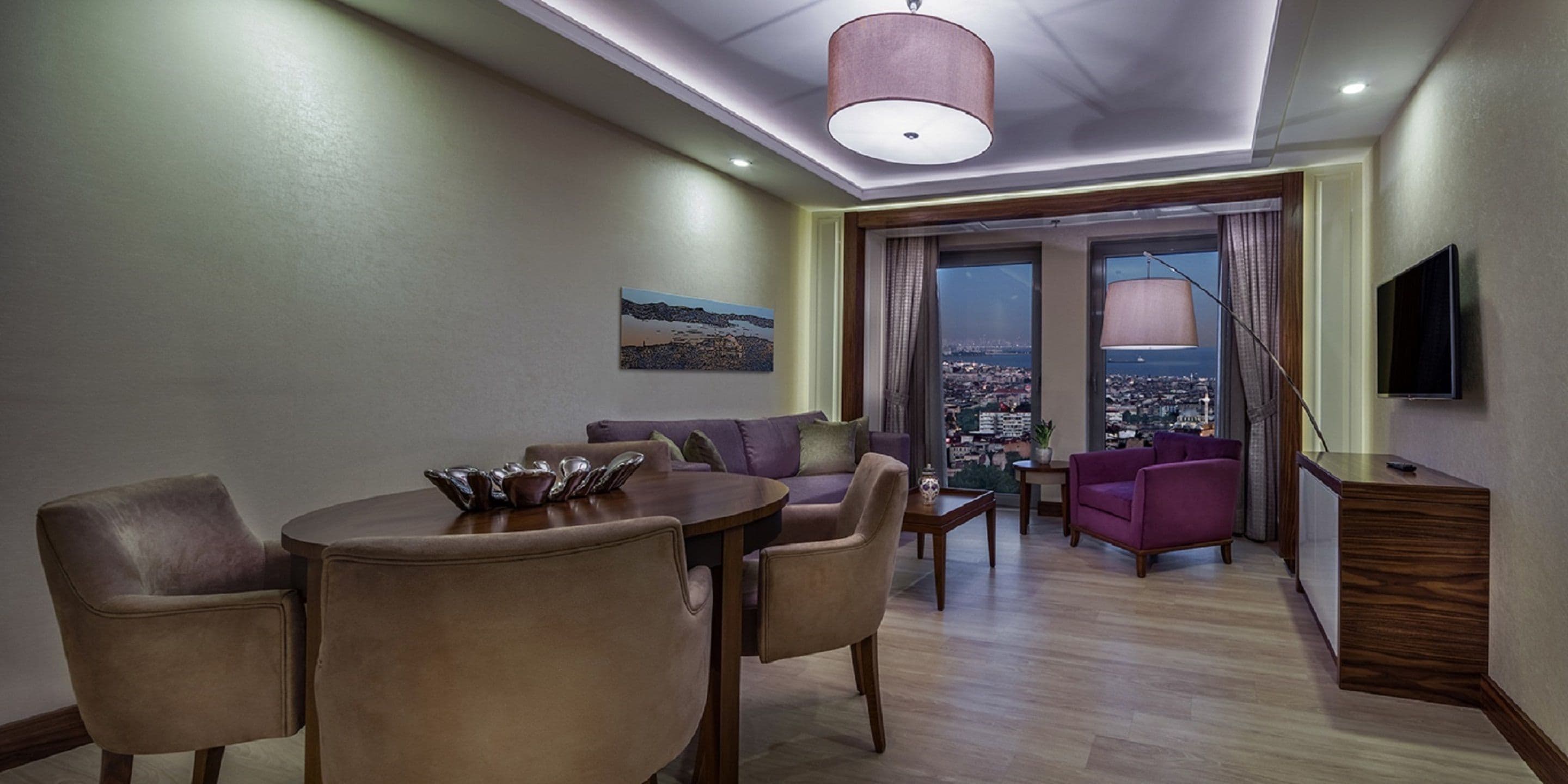 Sala de estar moderna com área de jantar, grandes janelas com vista para a cidade e uma televisão de tela plana em um armário de madeira.