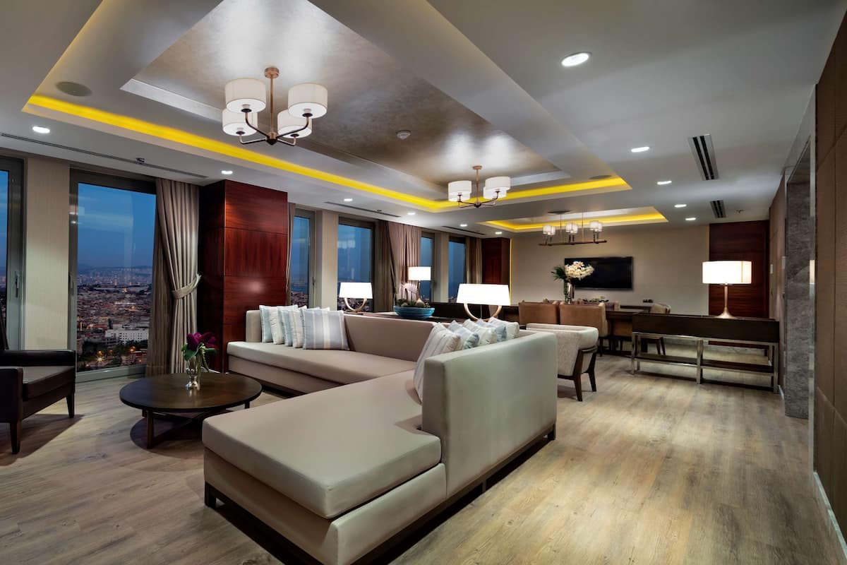 Quarto de hotel moderno com sofá, poltrona e área de jantar.