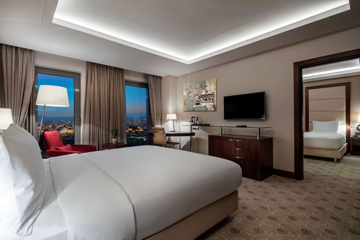 Quarto de hotel com uma cama grande, uma mesa de escritório, uma televisão e vista para a cidade.