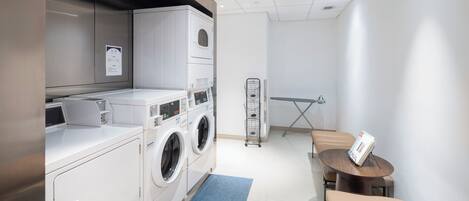 A modern laundry room with a washing machine, dryer, and a small table with a magazine.