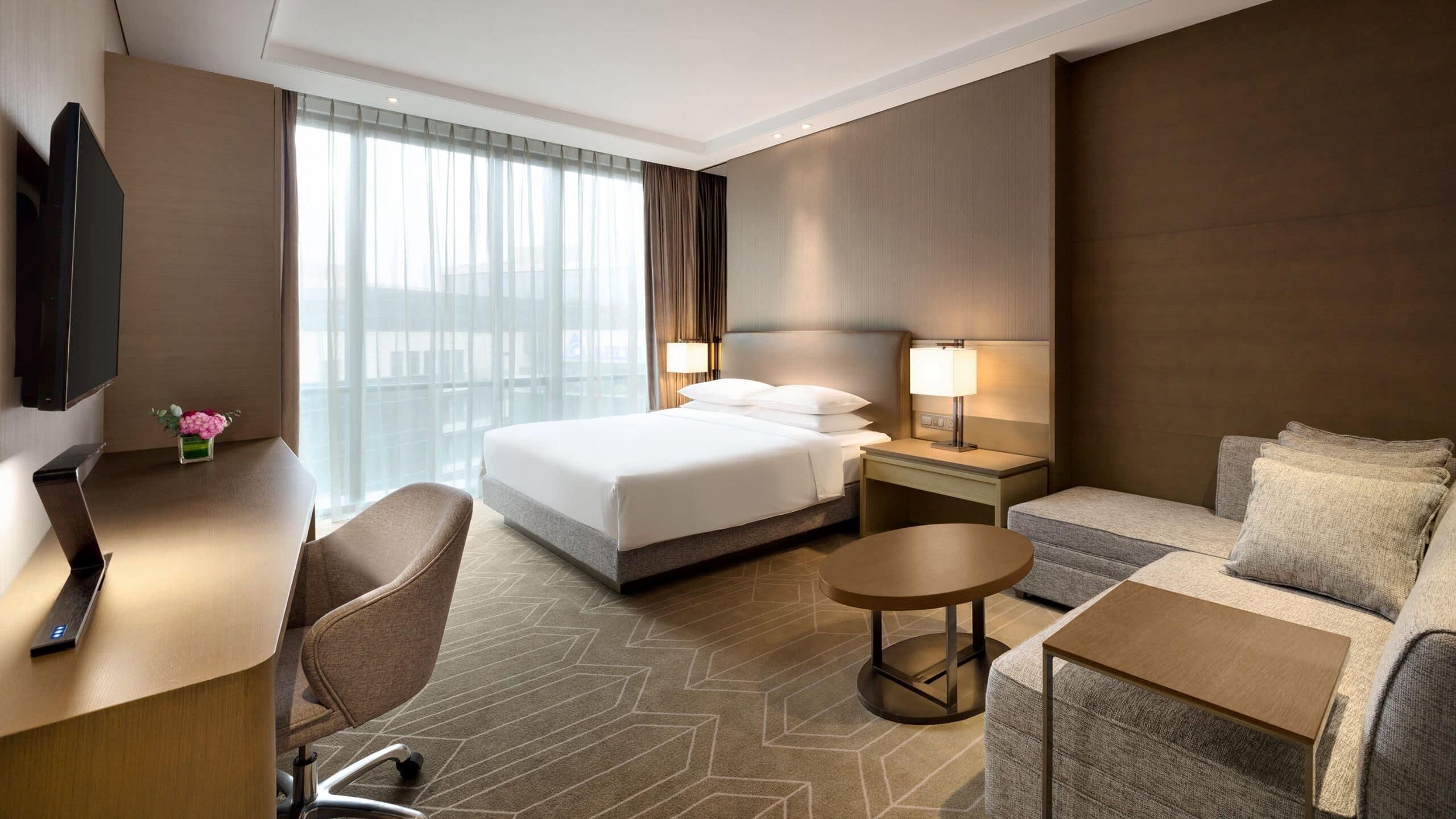 Een hotelkamer met een bed, een bureau, een stoel, een bank, een televisie en een raam met gordijnen.