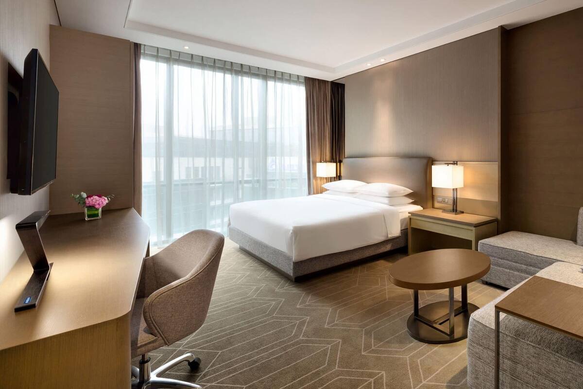 A hotel room with a bed, a desk, a chair, a sofa, and a TV.