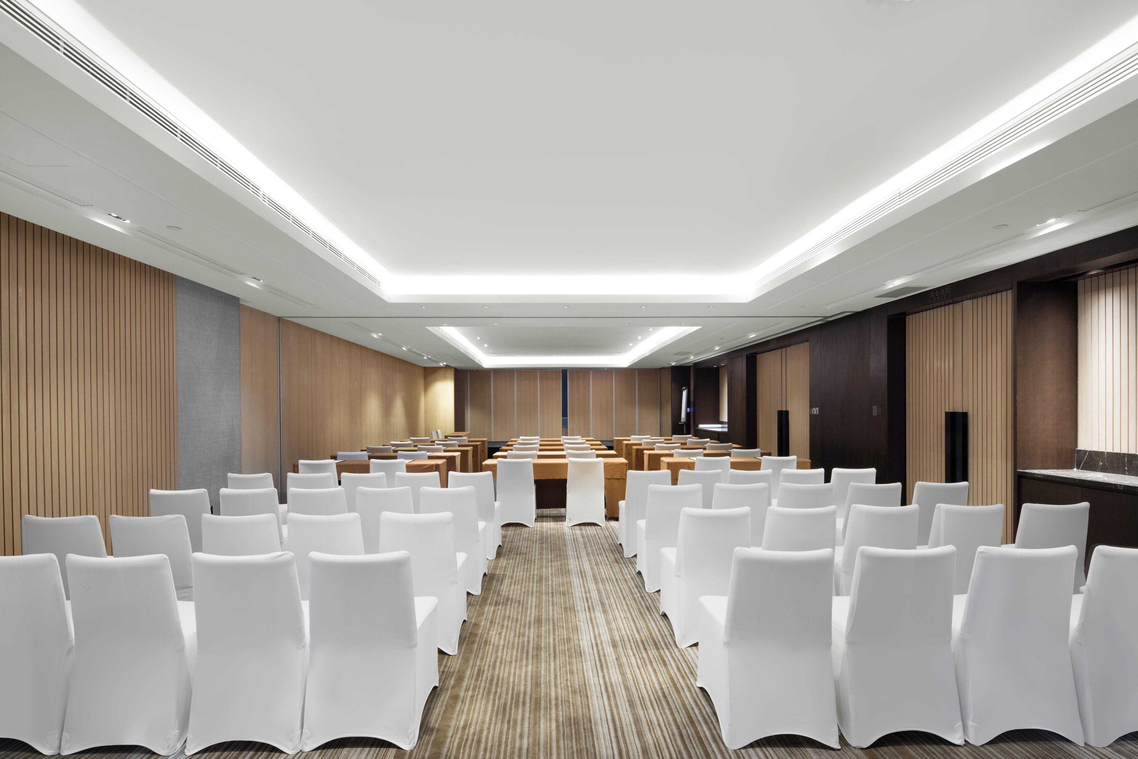 A conference room with rows of white chairs, a long table in the center, and a modern ceiling design.