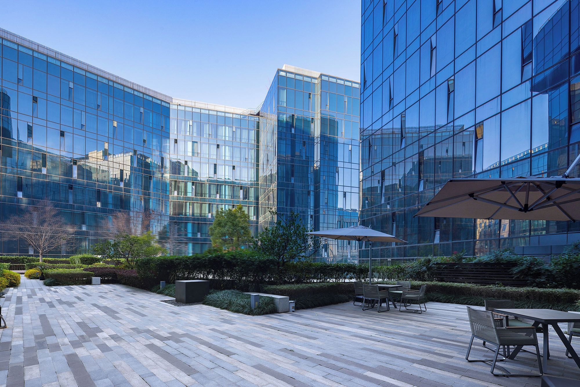 A modern building with reflective glass windows, outdoor seating, and a paved courtyard.