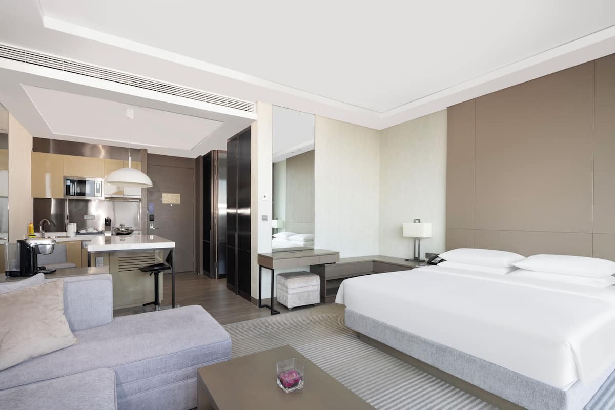 A hotel room with a bed, a sofa, a desk, a kitchenette, and a bathroom.