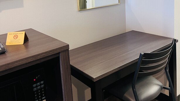 A hotel room with a wooden desk, a chair, a flat-screen TV, a mirror, and a non-smoking sign.