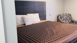 A neatly made bed with a patterned bedspread, a dark headboard, and a chair with a geometric pattern.