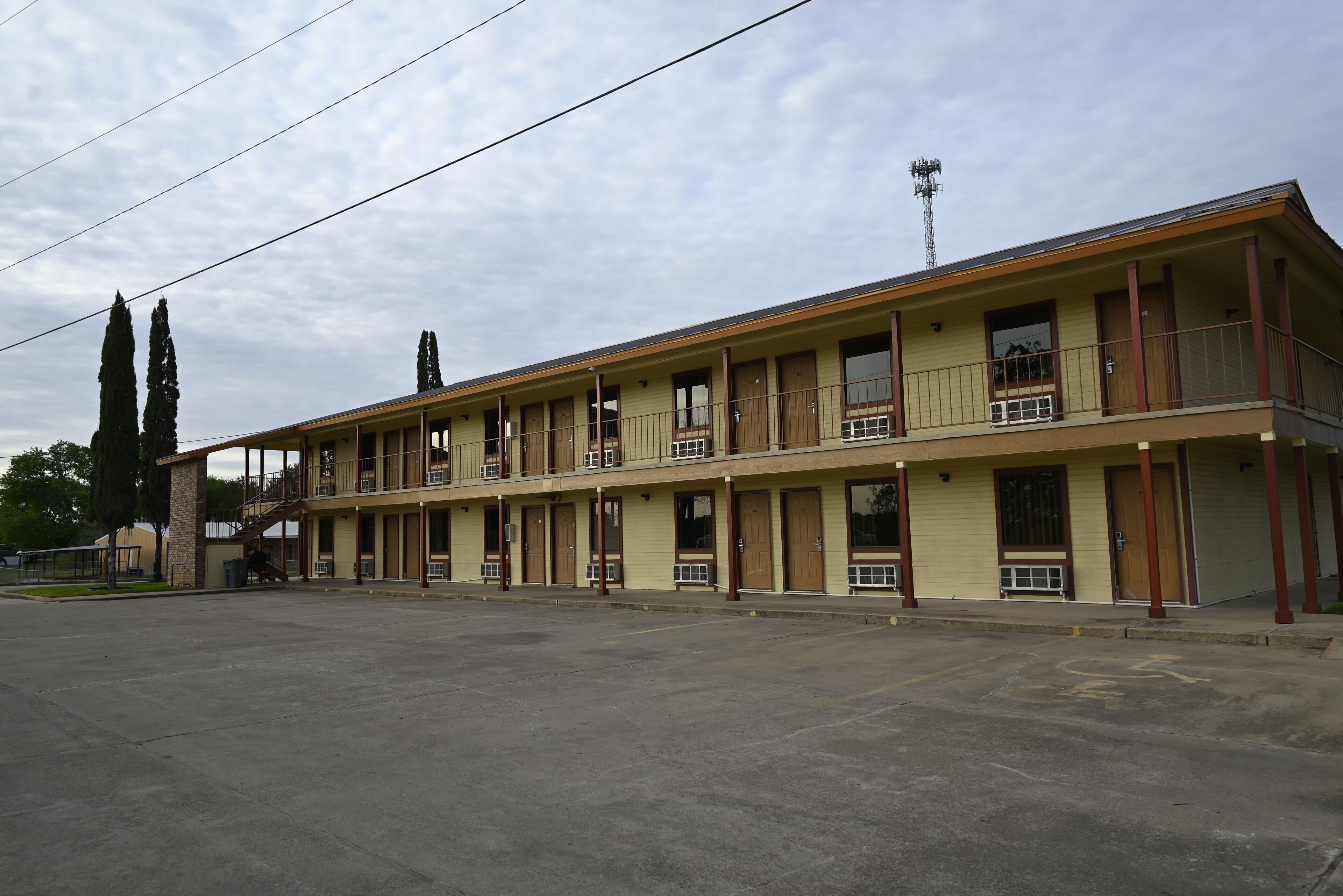 Un motel de dos pisos con pasillo central, ventanas amplias y estacionamiento.