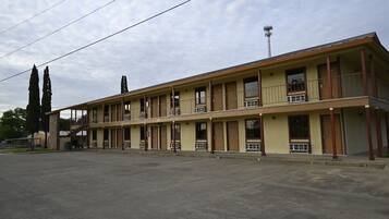 Un motel de dos pisos con pasillo central, ventanas amplias y estacionamiento.
