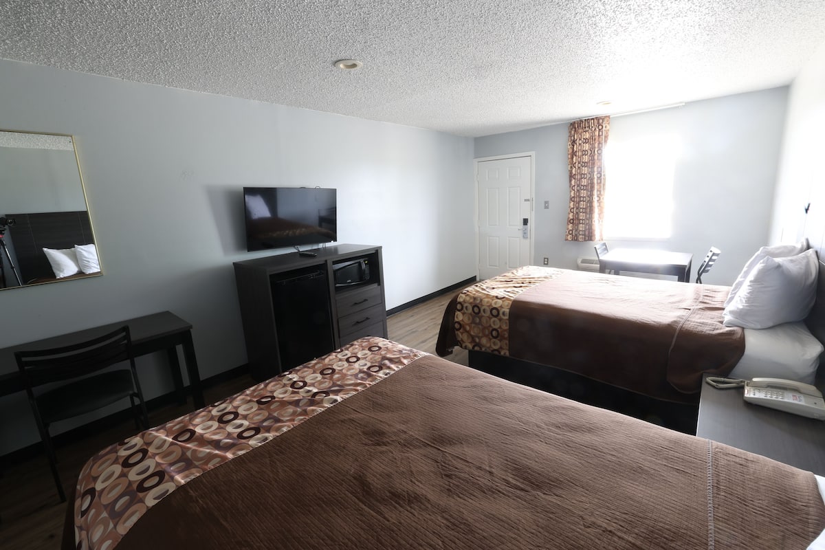 Habitación de hotel con dos camas, un escritorio, un televisor y una ventana con cortinas.