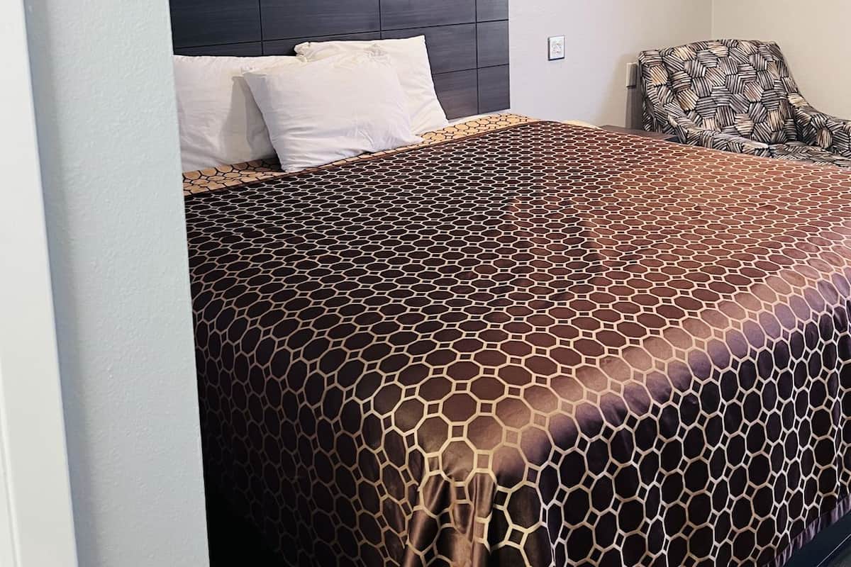 Un dormitorio con cama, cabecera, una silla y una lámpara de techo.