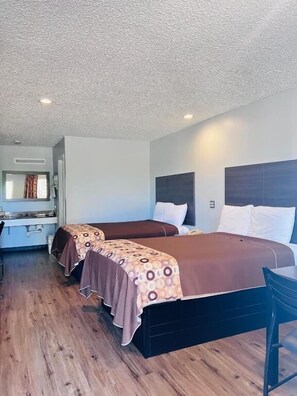 A hotel room with two beds, a wooden floor, and a small table.