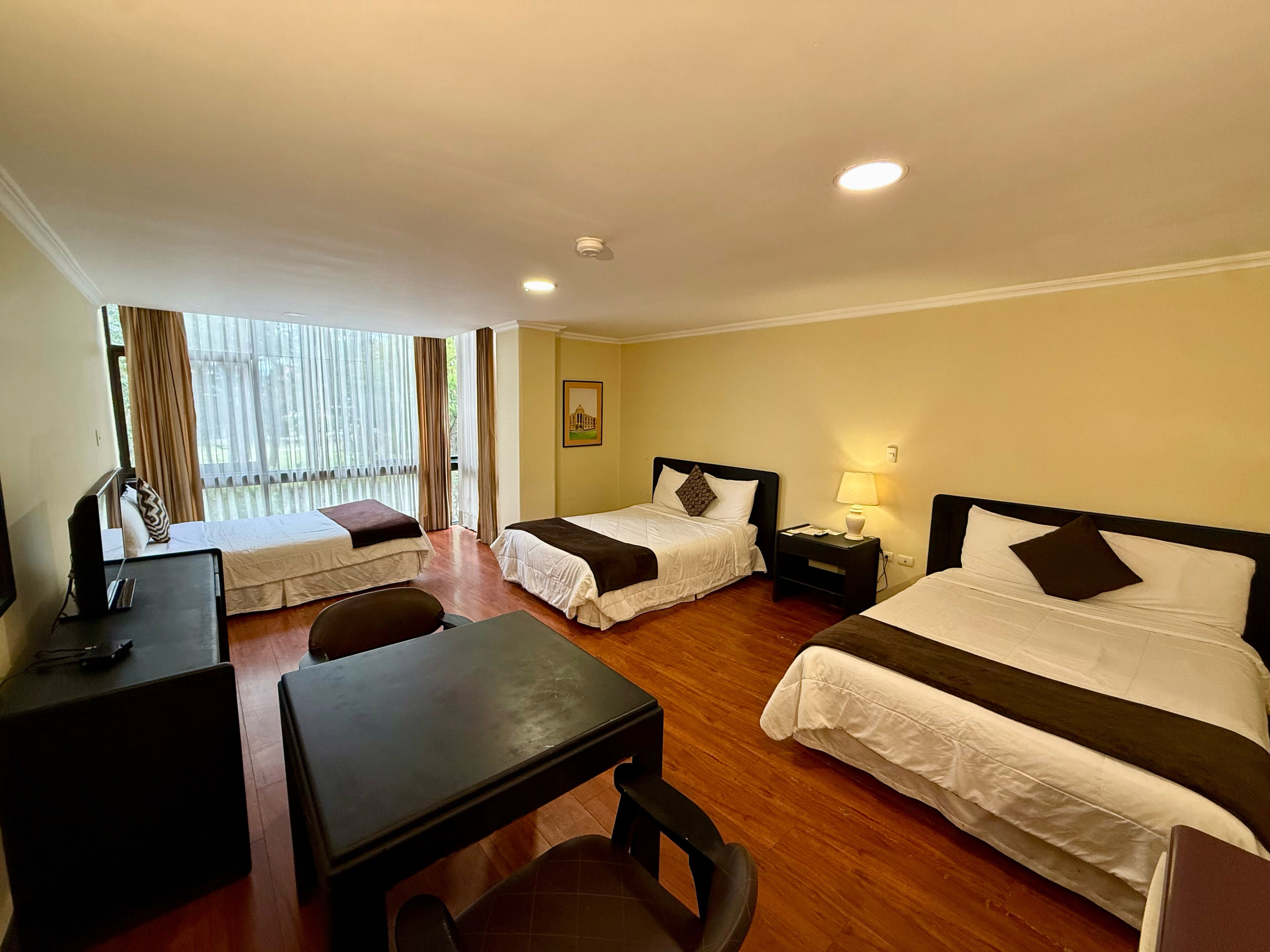 A hotel room with two beds, a desk, a chair, a table, and a window with curtains.