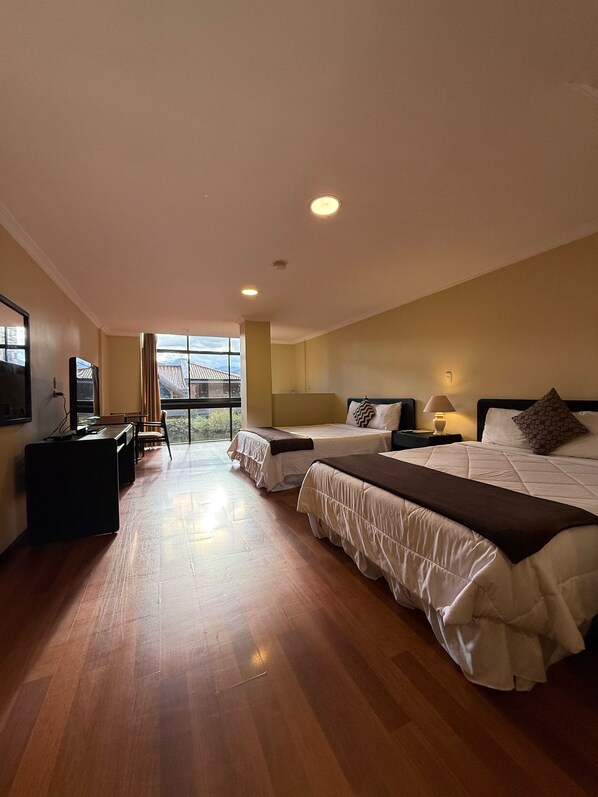 Habitación de hotel con dos camas, un escritorio, un televisor y un ventanal grande.