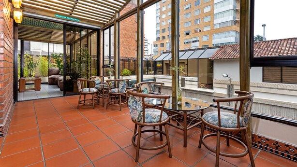 A covered outdoor seating area with chairs and tables, a brick wall, and a view of buildings. - NASS Pinar del Lago (Cuenca)