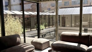 A modern living room with a glass coffee table, beige sofas, and large windows offering views of the street and buildings. - NASS Pinar del Lago (Cuenca)