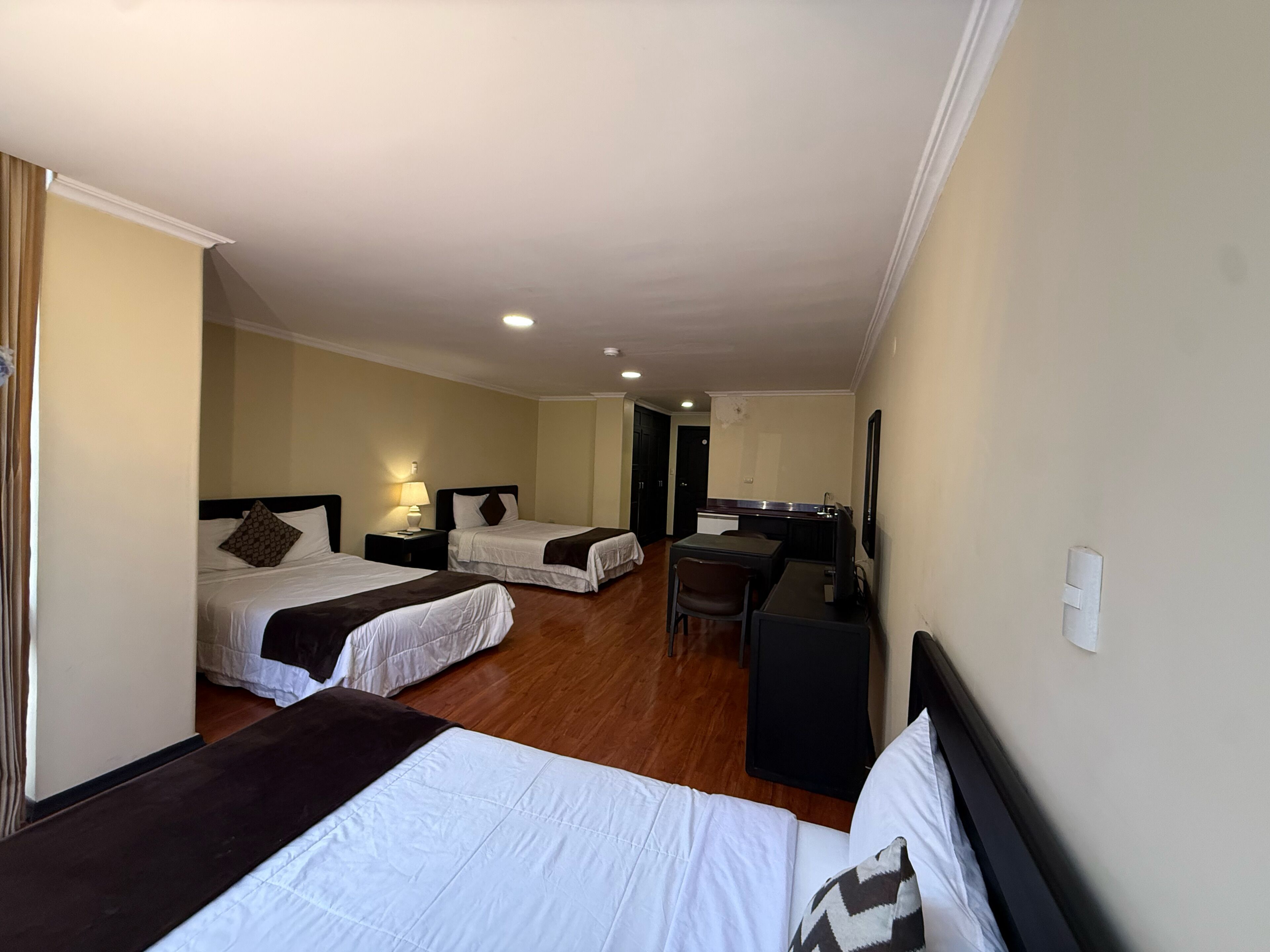 A hotel room with two beds, a desk, a chair, a television, and a small kitchenette.