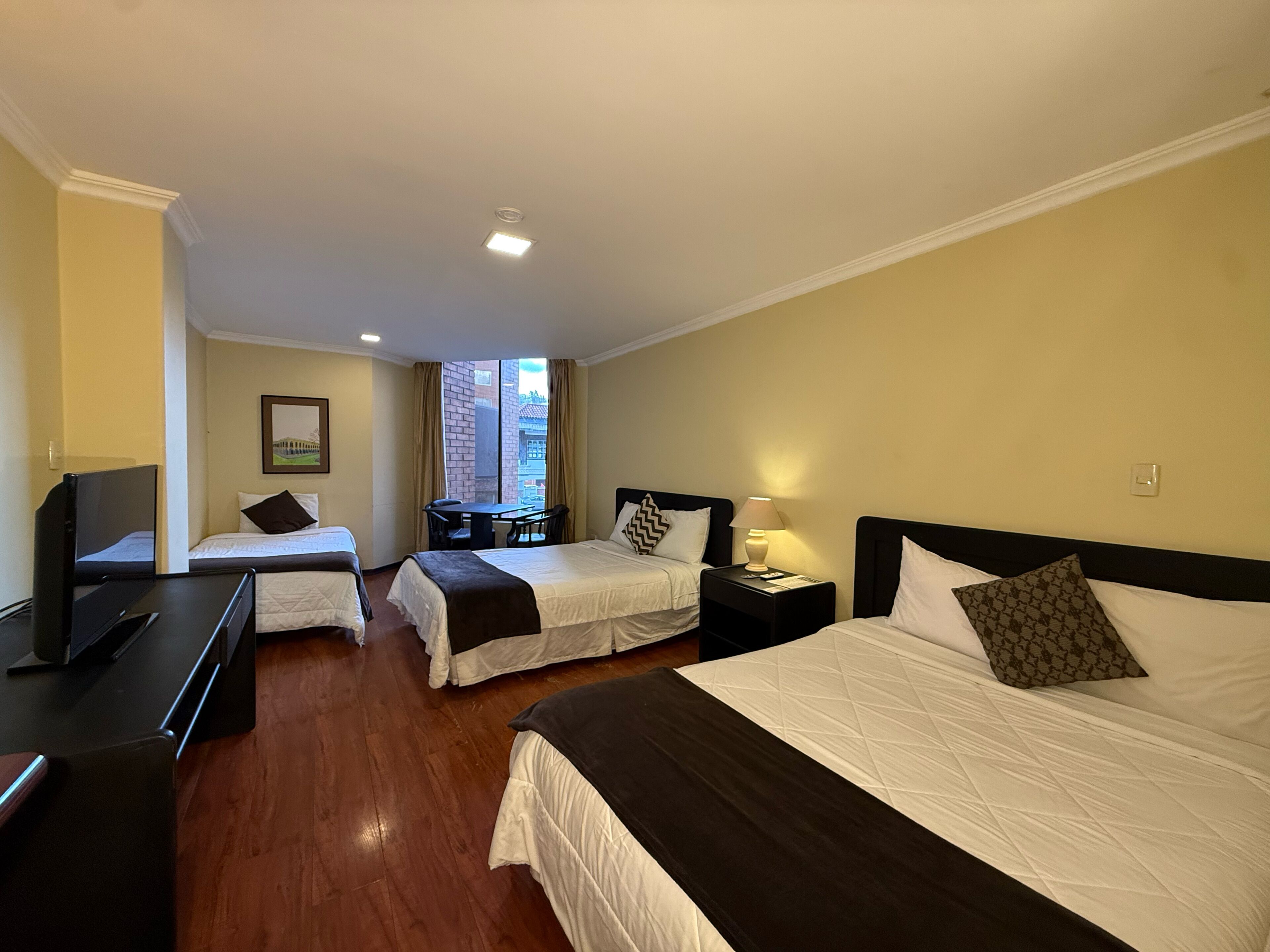 A hotel room with two single beds, a desk, a television, and a window with curtains.