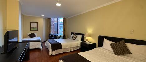 A hotel room with two single beds, a desk, a television, and a window with curtains.