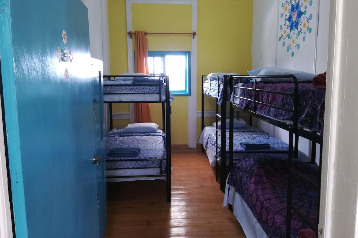 Une chambre de dortoir avec des lits superposés, un plancher en bois, une fenêtre avec des rideaux et une porte.