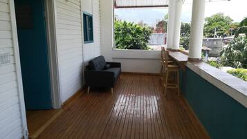Una habitación con piso de madera, sofá negro, ventana con vista a zonas verdes y pared blanca con puerta azul.
