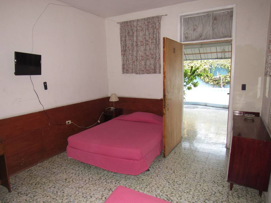 A room with a bed, a bedside table, a lamp, a TV mounted on the wall, and a window with a curtain.
