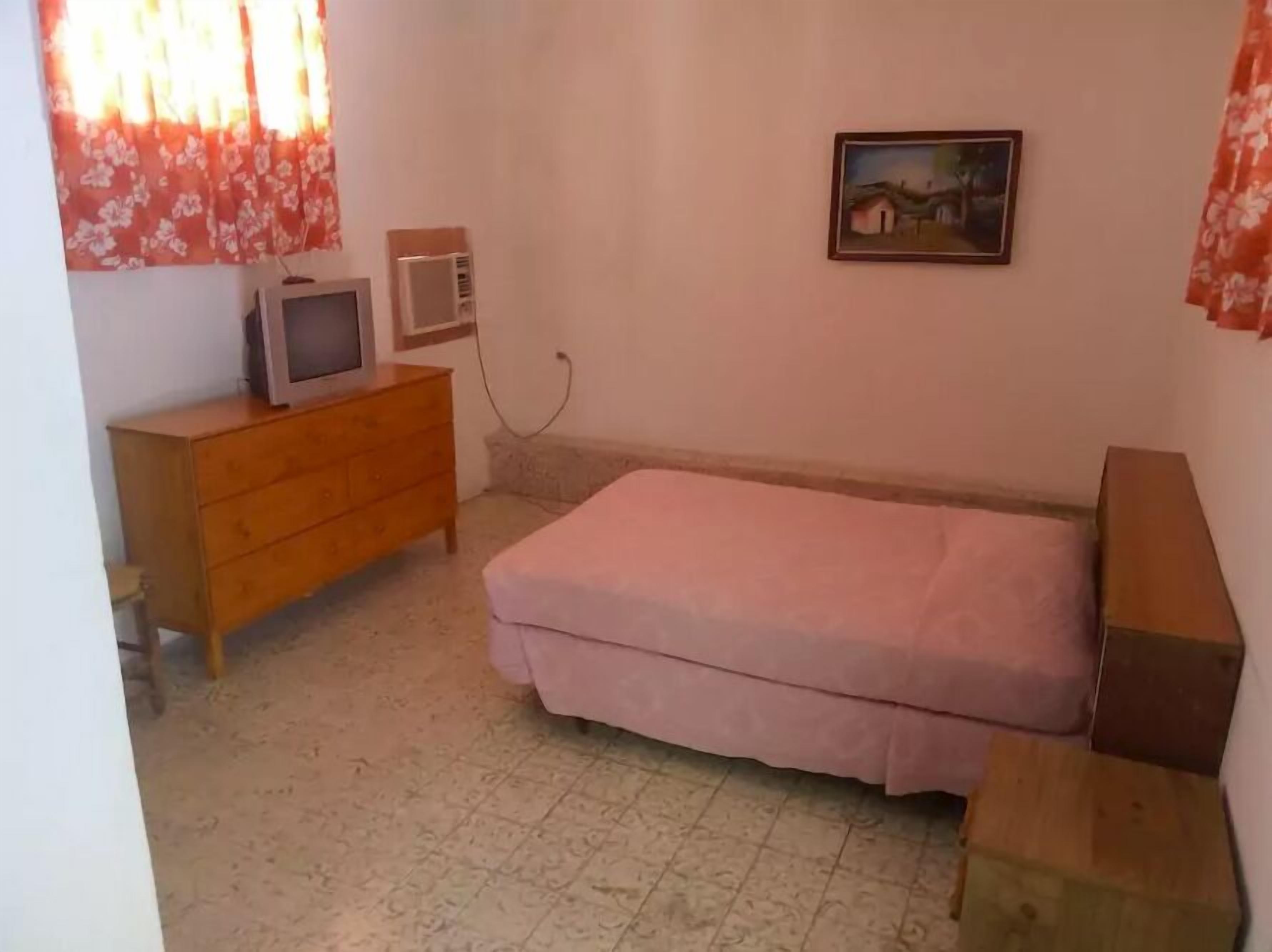 Ein kleines Schlafzimmer mit einem Einzelbett, einer hölzernen Kommode, einem Fernseher und einem Bild an der Wand.