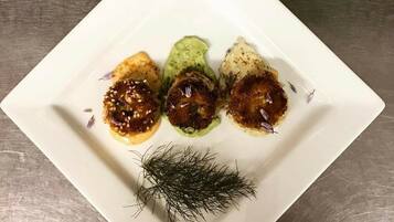 Een vierkant wit bord met vier stukken eten, versierd met dille en sesamzaadjes, op een metalen oppervlak.