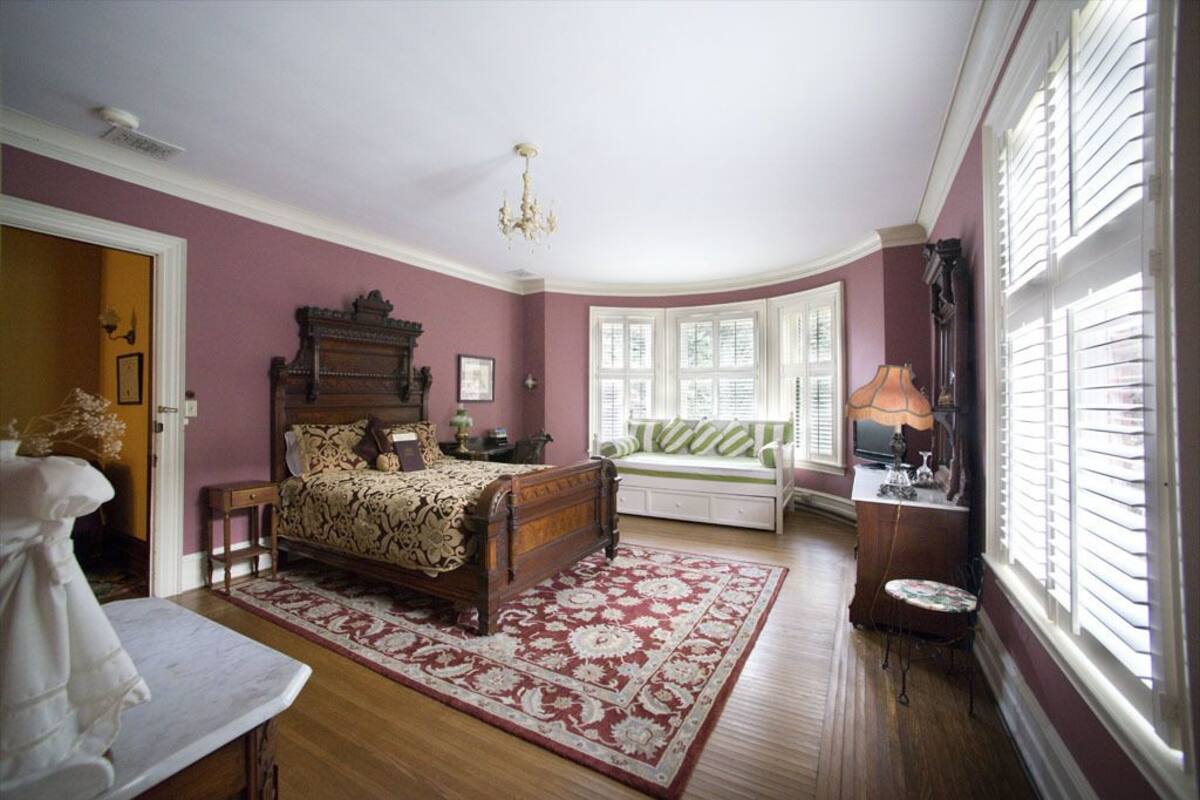 A bedroom with a wooden bed, a bench, a table, and a window with blinds.
