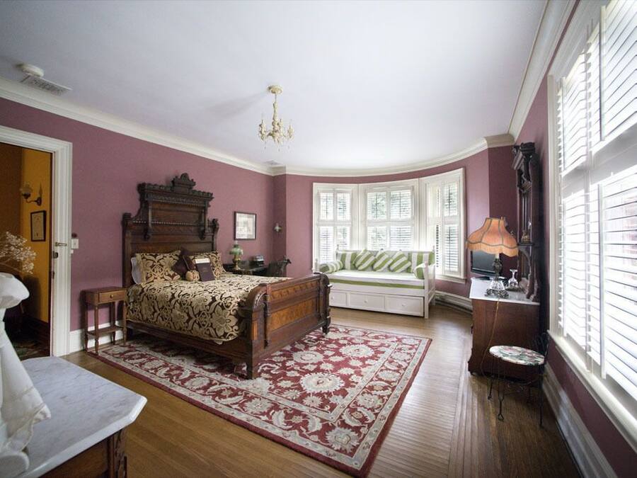 Une chambre à coucher avec un lit en bois, un banc, une table et une fenêtre avec des stores.