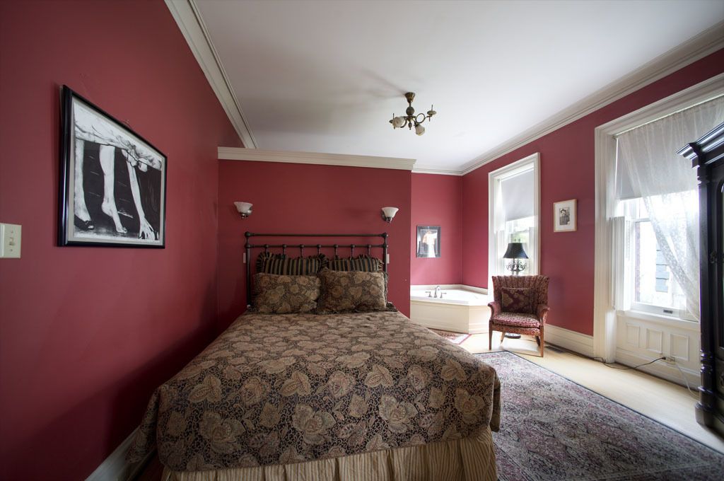 Ein Schlafzimmer mit einem großen Bett, einem Sessel, einem Nachttisch, einem Fenster und einer Kandelaber.