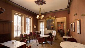 A dining area with marble tables and red chairs, a chandelier, and a fireplace. - The Peter Herdic Inn (Williamsport)