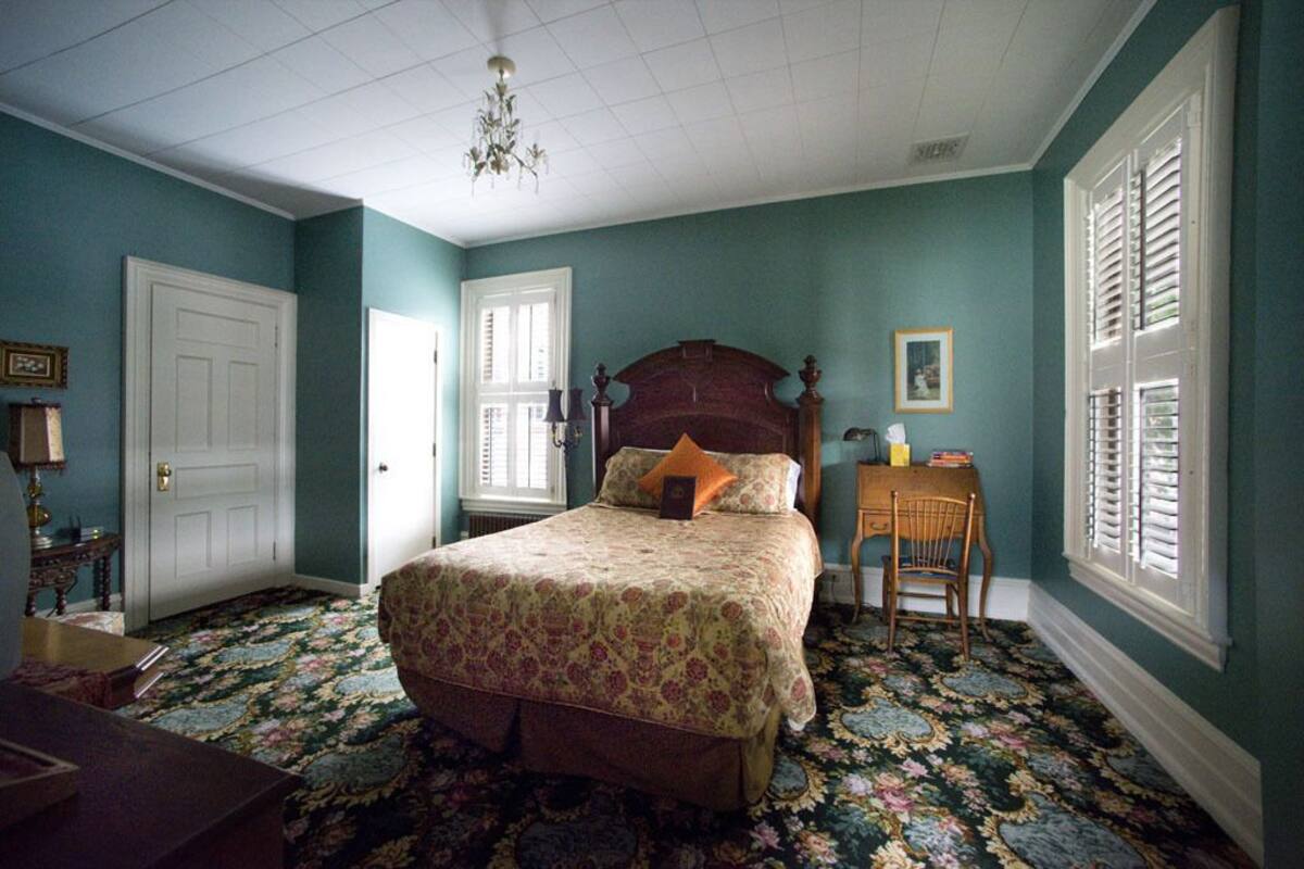 A bedroom with a large bed, a wooden nightstand, a chair, and a small table with a lamp.