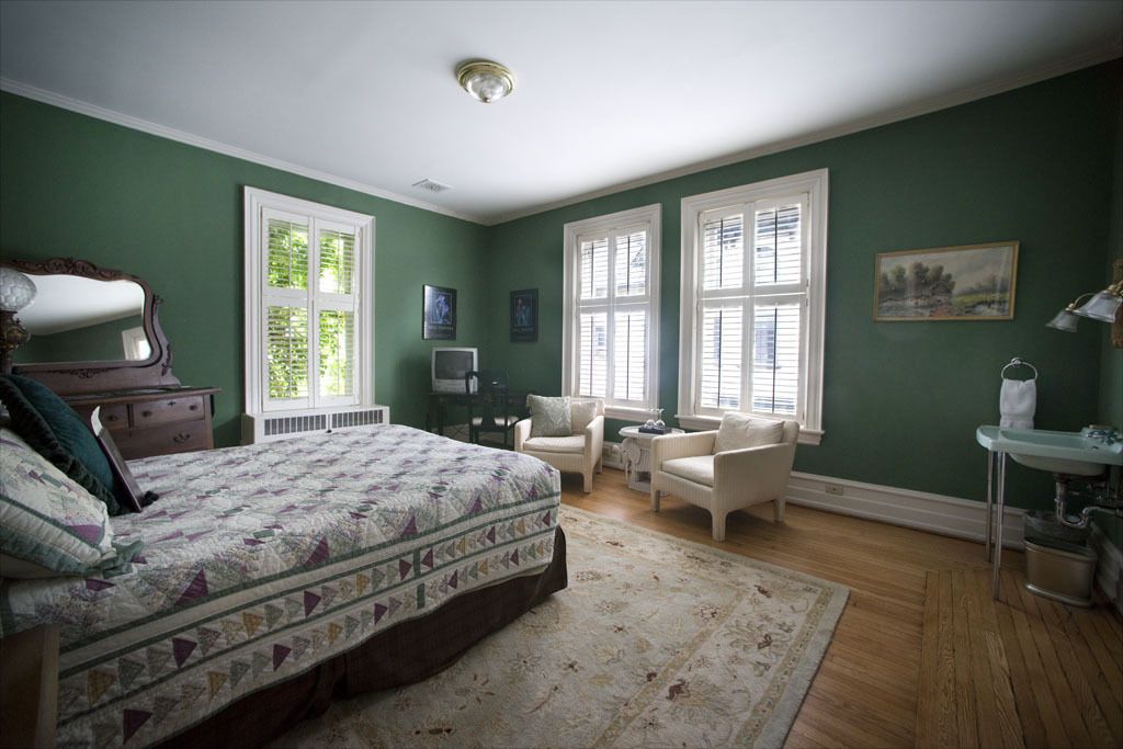 A bedroom with a large bed, two chairs, a desk, and a dresser.