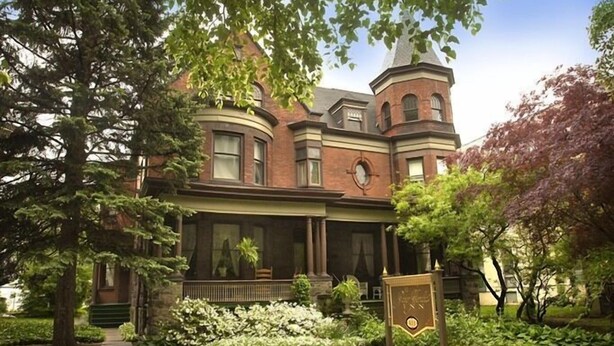 A historic brick building with a prominent tower, large windows, and a well-maintained garden with white flowering plants. - The Peter Herdic Inn (Williamsport)