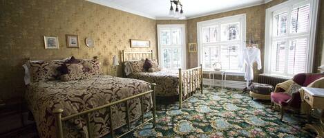 Una habitación con una cama grande, una cama más pequeña y una ventana con contraventanas.