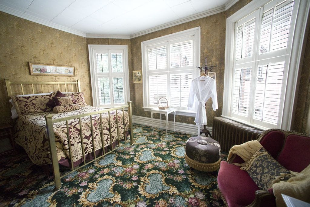 A room with a bed, a chair, a table, and a window with shutters.