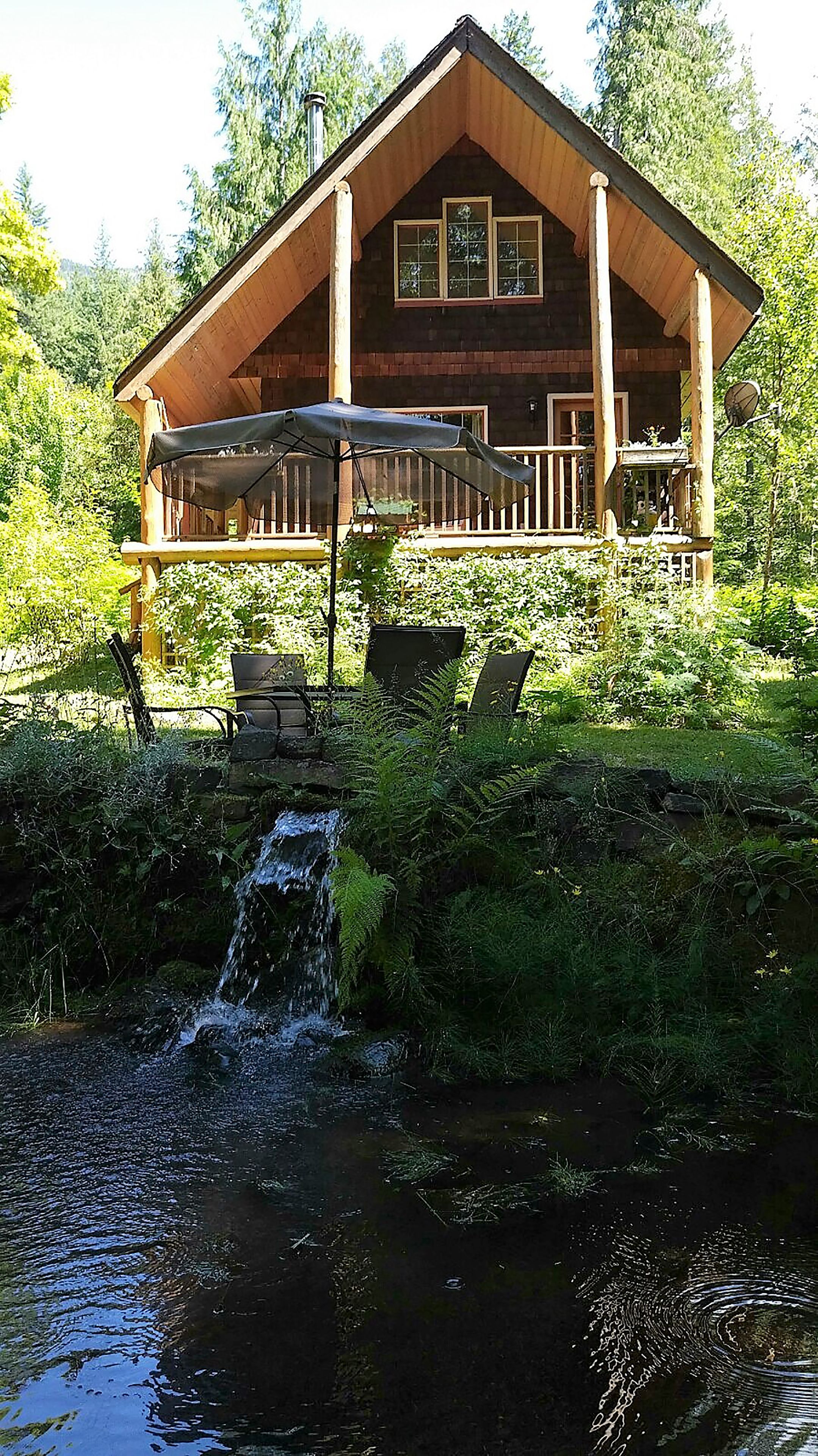 Una cabaña de troncos con porche, mobiliario exterior y una cascada.