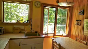 A kitchen with wooden cabinets, a sink, a clock, and large windows with a view of greenery. - Wedgwood Manor and Glamping Retreat (Crawford Bay)