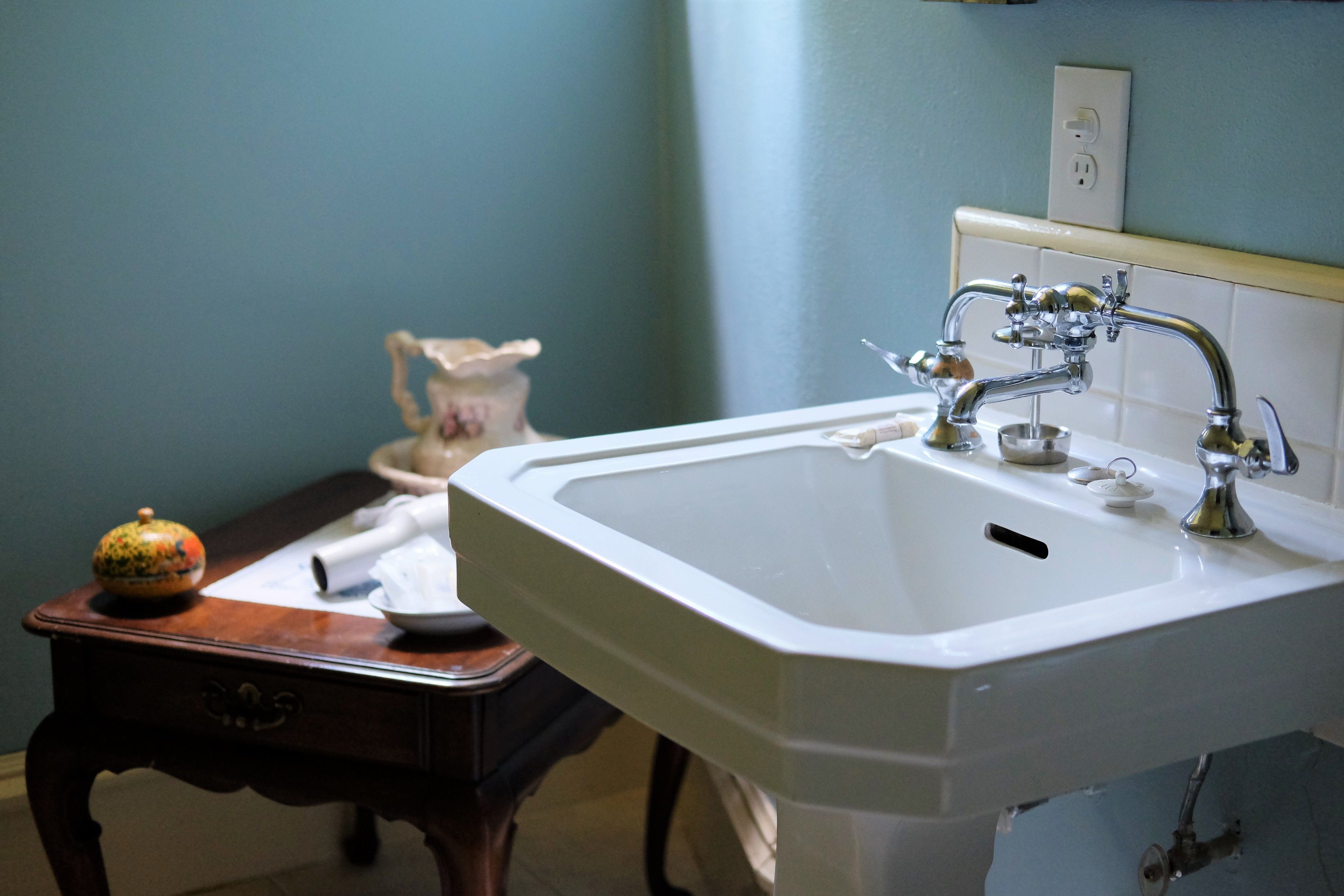 A bathroom with a white sink, a wooden table with a decorative item, and a vase.