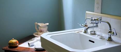 A bathroom with a white sink, a wooden table with a decorative item, and a vase.