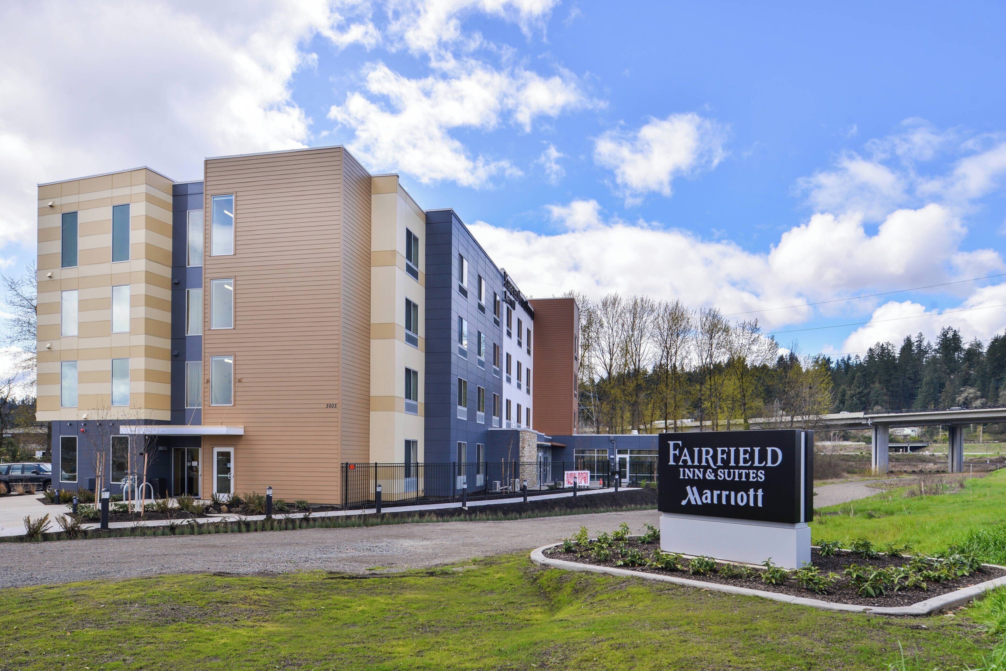 A multi-story Fairfield Inn & Suites Marriott hotel with a modern design, featuring a mix of beige and blue exterior walls, and a signboard in the foreground.