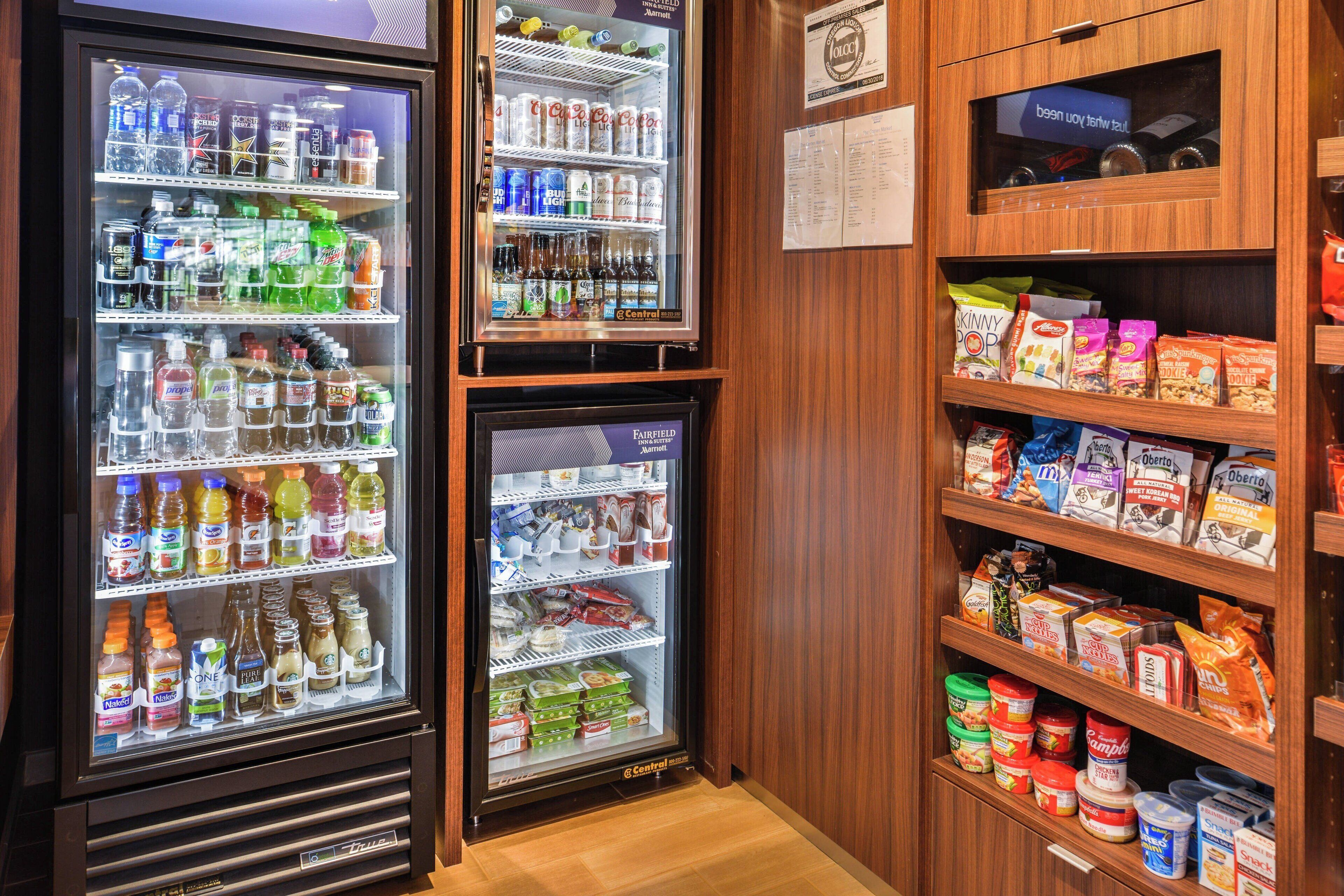 Un distributeur automatique proposant diverses boissons et collations, un réfrigérateur rempli de boissons et des étagères garnies de produits emballés.