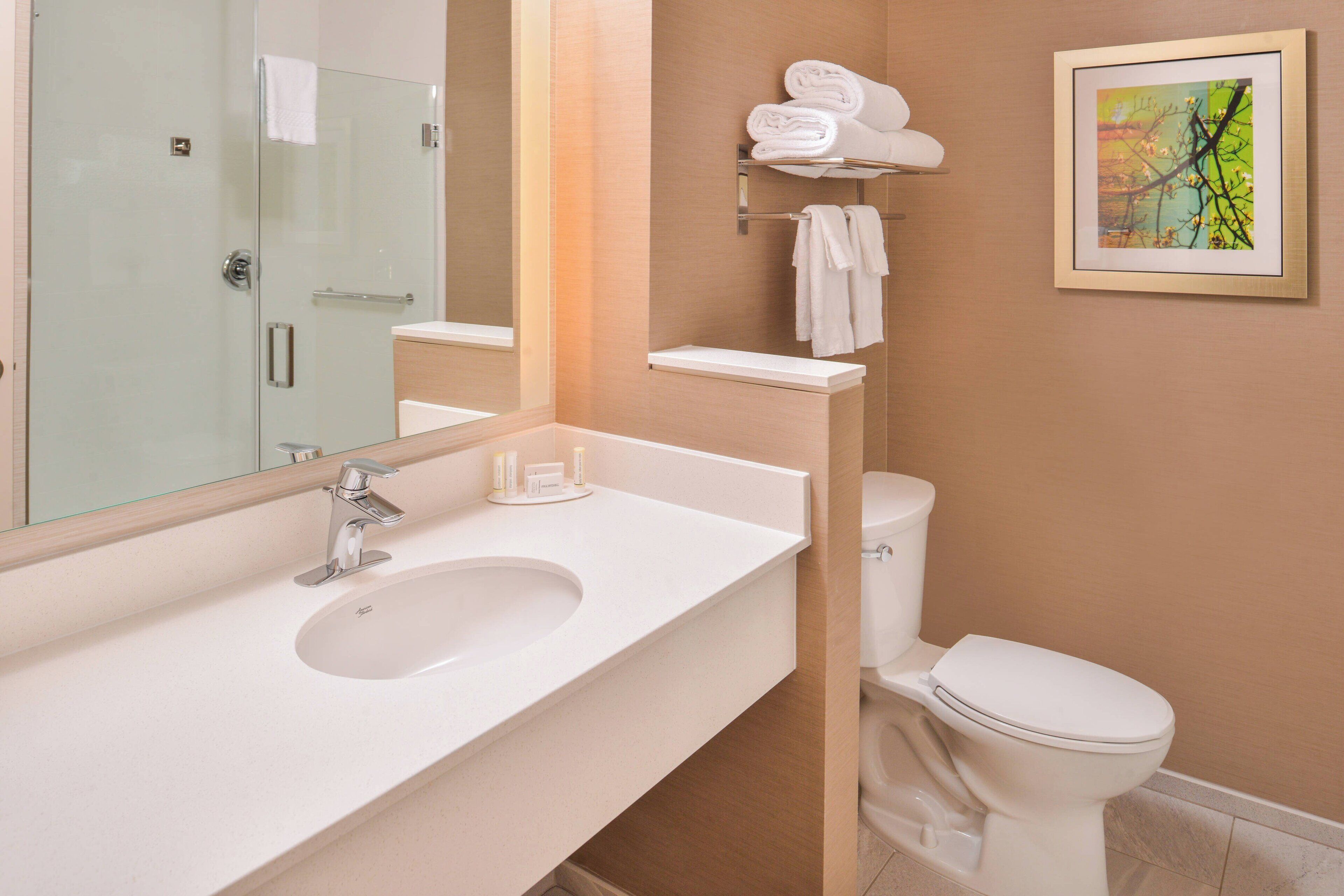 A bathroom with a white sink, a glass shower enclosure, a toilet, and a towel rack with folded towels.