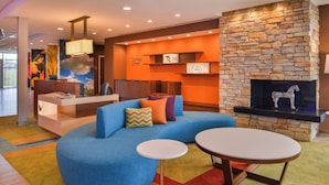 A modern lounge area with a blue sofa, a round table, and a stone fireplace. - Fairfield Inn & Suites by Marriott Eugene East/Springfield (Eugene)