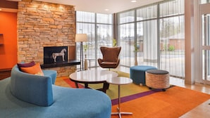 A modern lobby with a stone fireplace, blue seating, a round table, and large windows offering a view of the parking lot. - Fairfield Inn & Suites by Marriott Eugene East/Springfield (Eugene)