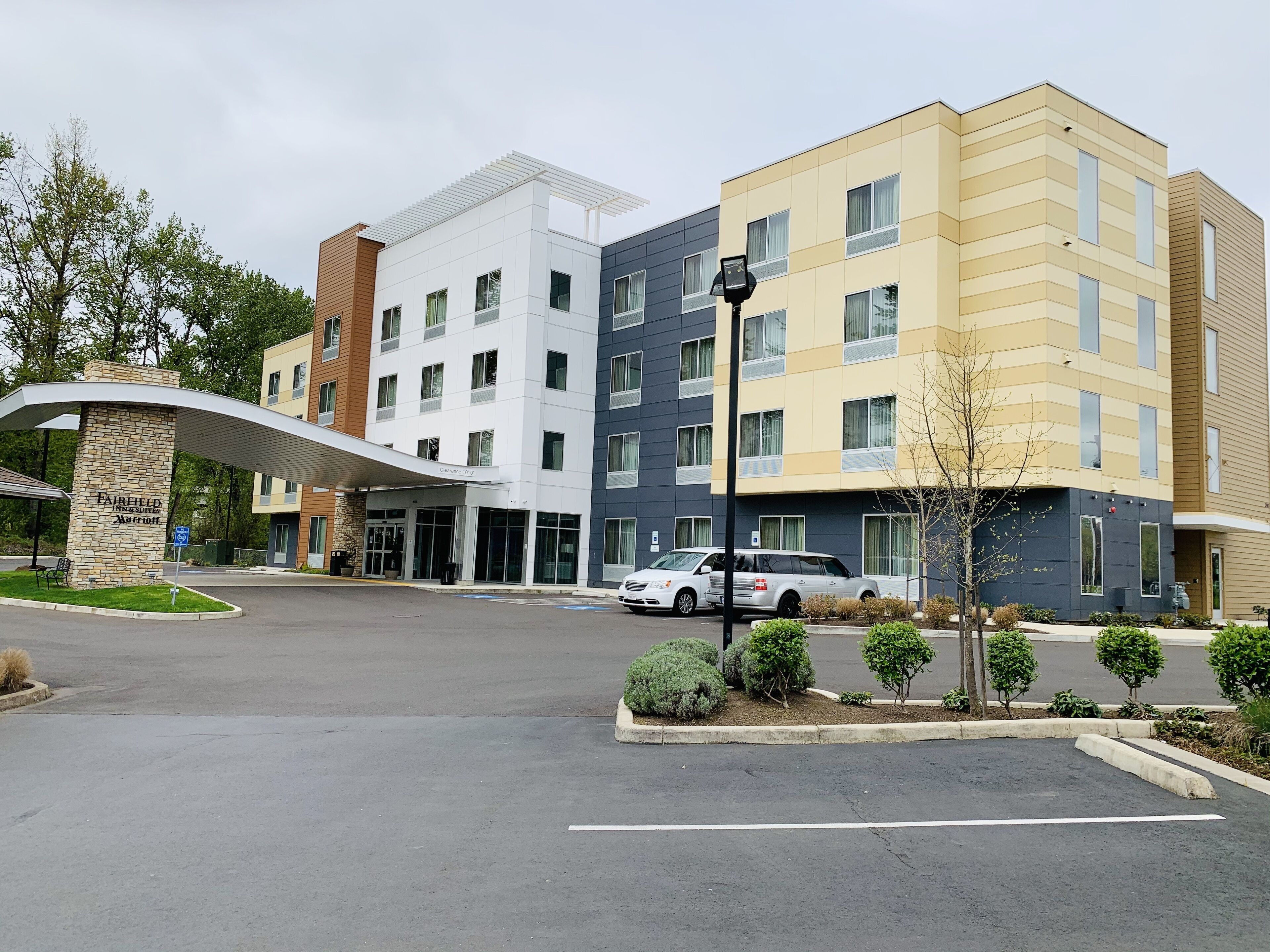 A multi-story hotel with a modern design, featuring a covered entrance and a parking area with several cars.
