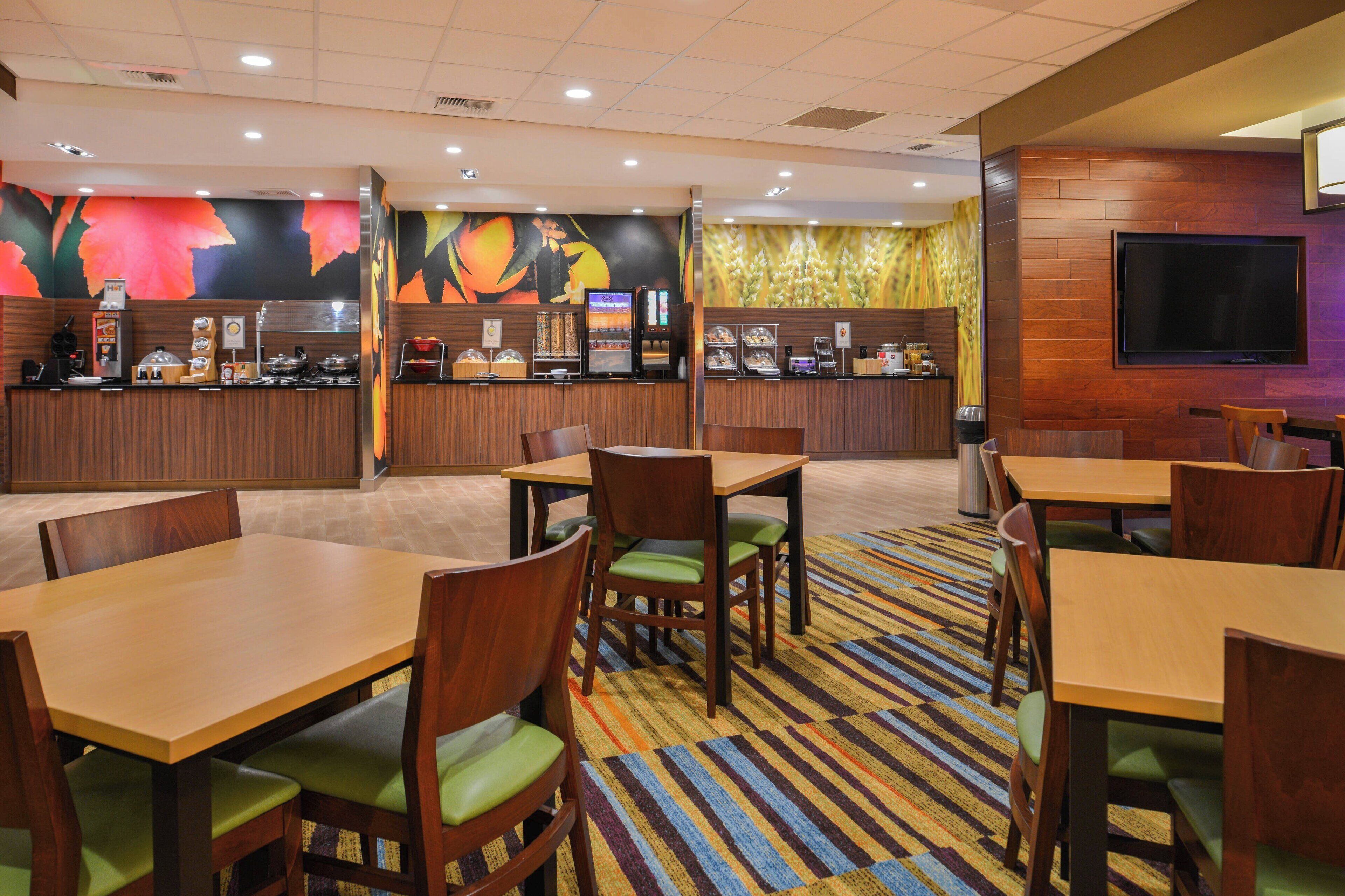 A restaurant with wooden tables and chairs, a counter with a coffee machine, and a TV mounted on the wall.