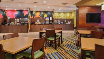 A restaurant with wooden tables and chairs, a counter with a coffee machine, and a TV mounted on the wall.